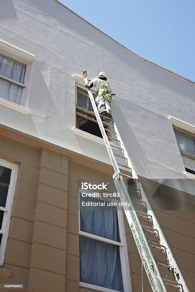 Man painting wall on tall ladder "Cape Town, South Africa - January 30, 2012: African man in downtown Cape Town painting a wall on the top of a tall ladder" High Up Stock Photo