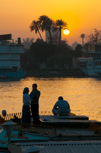 Cairo, Egypt - March 5, 2011: A young Egyptian couple and a lone man are beside the Nile River at sunset in downtown Cairo.