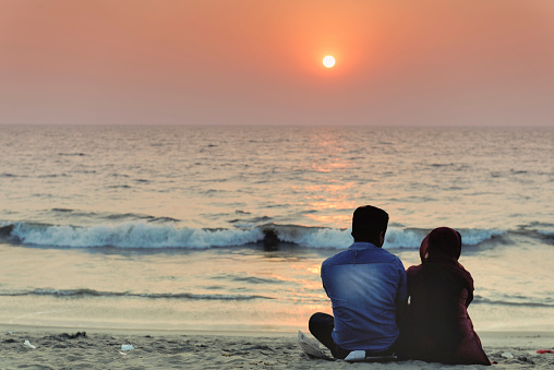 Kozhikode, Kerala,India - January 16 , 2013: Couple sitting on the Calicut Beach and enjoying a beautiful sunset. Kozhikode, formerly known as Calicut, is a city on the Malabar coast in southern India.