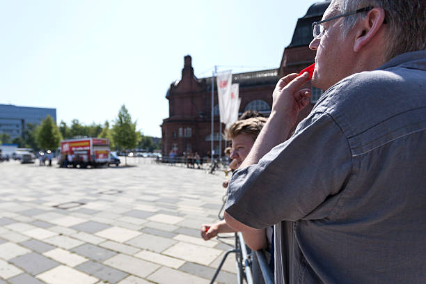 Counterprotestors against Neonazi speech "Wiesbaden, Germany - July 27, 2012: A middle-aged protestor against Neonazi speech in the city center of Wiesbaden, Germany, with a red whistle behind a barrier. Protestors tried to drown out the speech of the Neonazis with whistles and music. In the background on the center of the town square the NPD truck. Founded in 1964 the NPD is a German nationalist party, its agitation is racist, antisemitic, revisionist. Because of its activities against the constitutional order the party is under observation of the Verfassungsschutz (German Federal Intelligence agency)" national democratic party of germany stock pictures, royalty-free photos & images