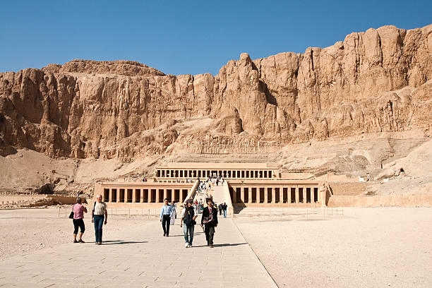 Temple of Hatchepsut in Deir el-Bahari "Luxor, Egypt - November 21st, 2011: This is a front view of Temple of Hatchepsut in Deir el-Bahari which is located at the bottom of Theban Hills nearby Luxor. Tourists are coming back from visiting the temple. This photo was taken from the yard at the first terrace\'s level in the temple." el bahari stock pictures, royalty-free photos & images