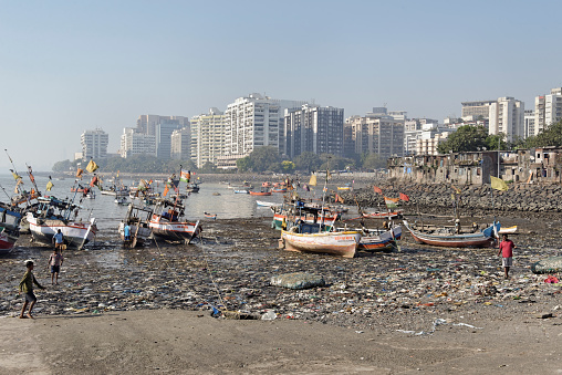 Mumbai,Maharashtra, India - January 23, 2013: Contrast in the city between the modern apartment buildings and the fishermen's houses - some have satellite TV and internet - on Back Bay in south Mumbai. Local fishermen are walking on the heavely polluted beach with fishing boats at low tide. 