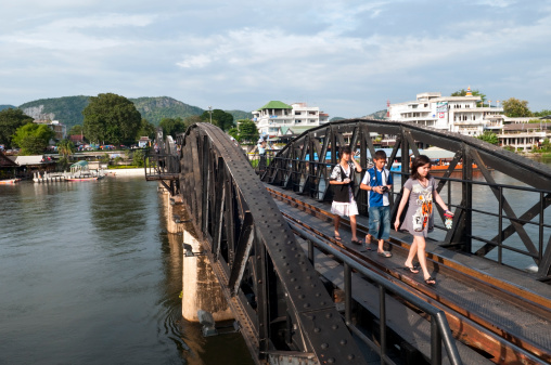 Kanchanaburi, Thailand - October 3, 2011: Thai young people walk across the famous Bridge on the River Kwai, built by Allied POW labor during World War II. The bridge is part of the Death Railway.