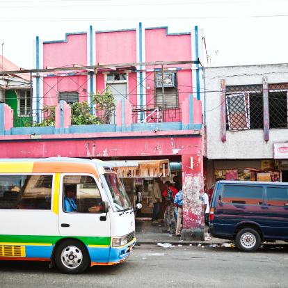 Kingston, Jamaica - January 20, 2012: Colorful minibus driving in front of colorful buildings in Kingston downtown near the market area. People in background.