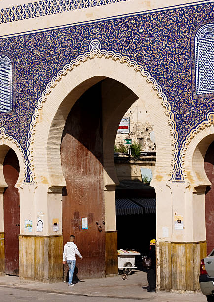 Bab Boujeloud gate, Fez, Morocco "Fez, Morocco - February 6, 2013: Young man entering the famous Bab Boujeloud gate of Medina in Fez. It's covered with blue ceramic tiles painted with flowers and calligraphy." bab boujeloud stock pictures, royalty-free photos & images