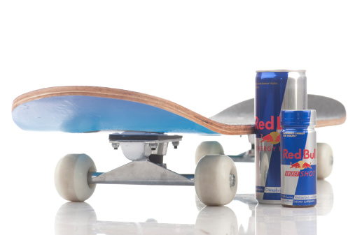 Belgrade, Serbia - January 28th, 2012: 250 ml Red Bull drinks standing with skateboard isolated on white background. Red Bull is well known energy drink.
