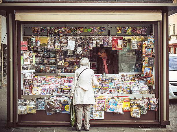 Elder Woman Buying Magazine at Italian News Stand "Ferrara, Italy- October 7, 2012: Elder Woman Buying newspapers at a news stand while the clerk is serving her." news stand stock pictures, royalty-free photos & images