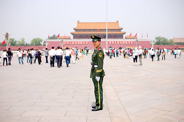 Beijing, China - May 6, 2008: Young Chinese soldier standing in uniform and looking at camera on the Tiananmen Square in Beijing. Local people walking around him.