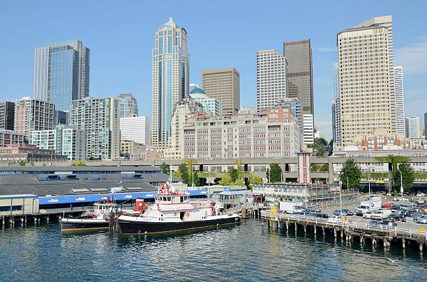 Seattle Waterfront "Seattle, USA - September 8, 2011: The Seattle waterfront as seen from Puget Sound with boats of the fire department in the foreground. Some of the many tourists who visit can be seen here enjoying shops, restaurants, or a variety of boat ride options offered to them via various local cruise operators." ferry terminal audio stock pictures, royalty-free photos & images