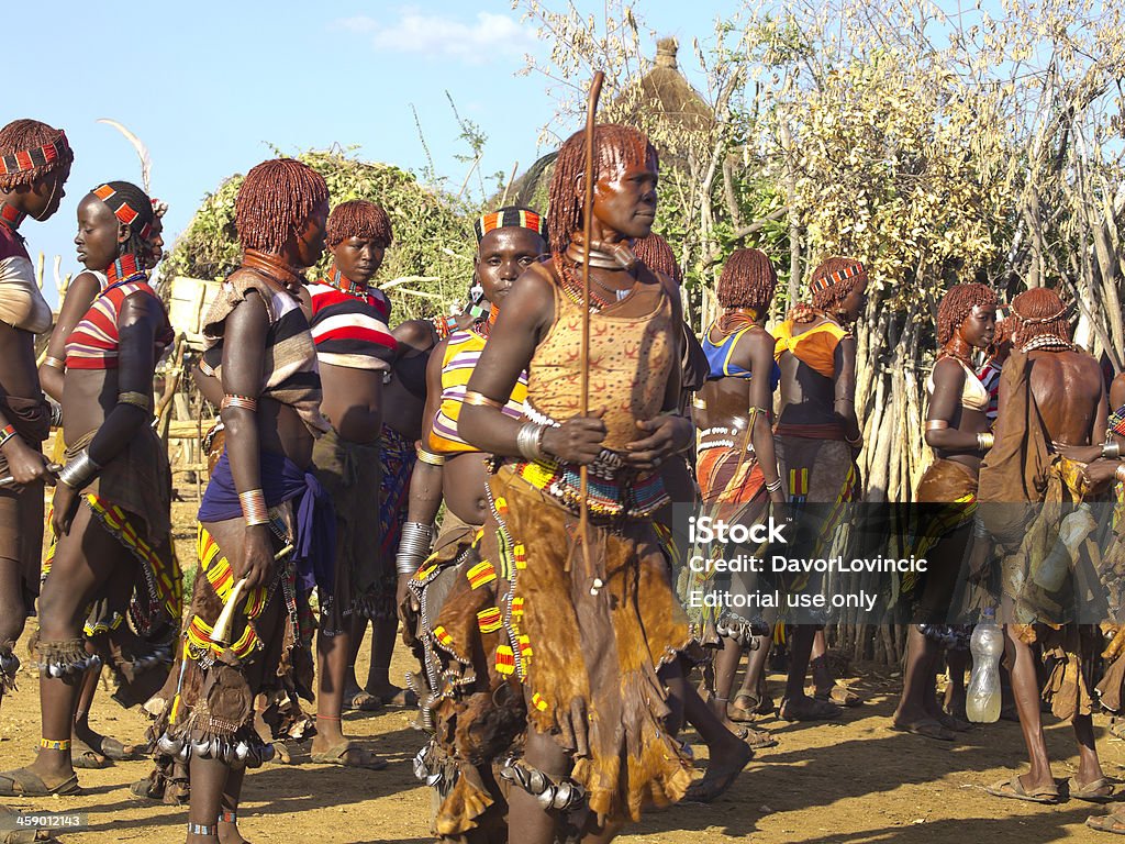 Hamer Dance "Turmi, Ethiopia- November 3, 2012: A lot of Hamer woman in traditional, every day  clothes dancing close together in house backyard reserved for cattle. In background, around is the natural, rural vegetation, roof of local house and the blue sky." Adult Stock Photo