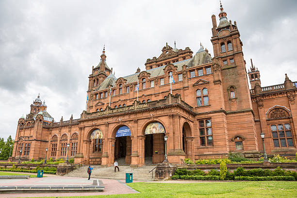 Glasgow, UK - July 13 2025: Visitors admire the grand Spanish Baroque facade of the iconic Kelvingrove Art Gallery and Museum, a famous cultural landmark made of red sandstone under a cloudy sky
