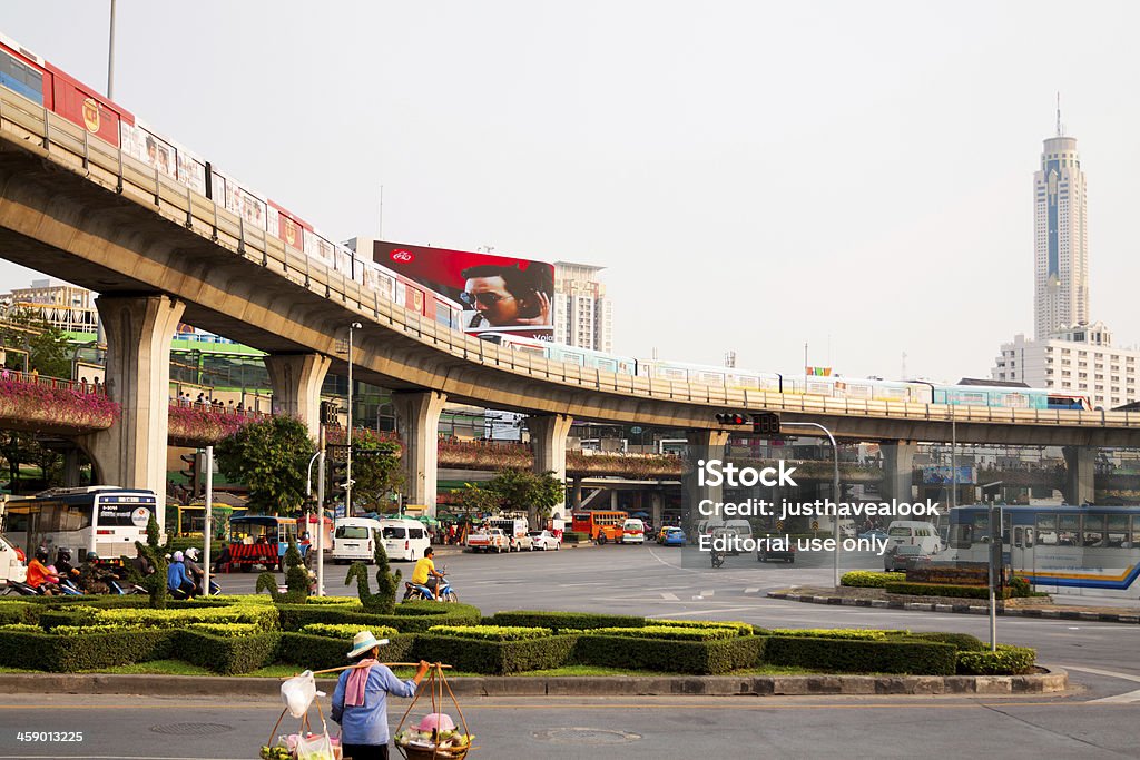 Skytrains around square Ratchachewi "Bangkok, Thailand - February, 18th 2013: Skytrains around square Ratchachewi, main square with Victory Monument and many shopping centers around. In roundabout is some traffic. Below skytrains are walking people on airbridges and in foreground is a food seller crossing street." Architecture Stock Photo