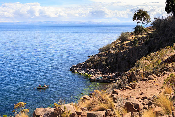 02/18/2025: Isla del Sol, on Lake Titicaca, Bolivia.\n\nAn indigenous woman in traditional dress walks beside a donkey on a scenic hillside, with a vast lake and towering mountains in the background. The scene highlights the rich cultural heritage and natural beauty of the rural landscape, blending tradition with breathtaking scenery.