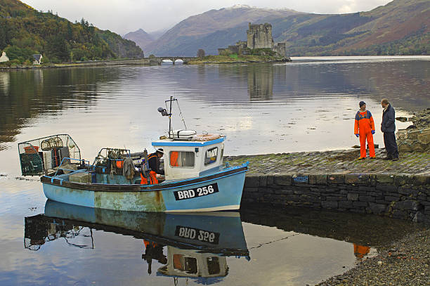 Eilean donan castle stands by a loch in the rugged scottish highlands, its historic stone walls rising under a dramatic, cloudy sky and reflecting the moody atmosphere of the landscape