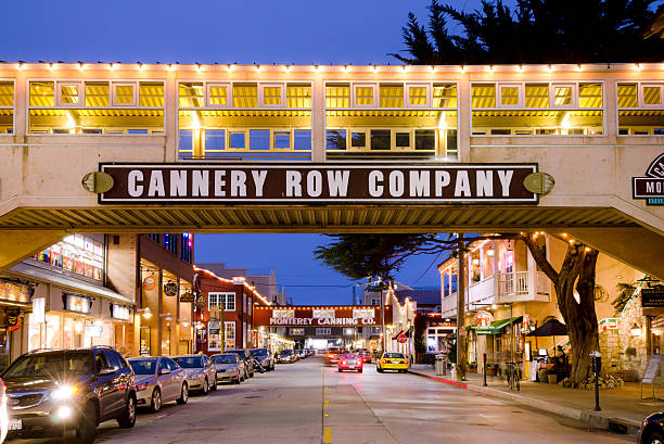 Cannery Row in Monterey, CA at night "Monterey, United States - July 1, 2012: Cars drive along the waterfront street of Cannery Row in the New Monterey section of Monterey as a woman sits in a chair along the sidewalk nearby. The area is the site of a number of now-defunct sardine canning factories, the last of which closed in 1973. Now, Cannery Row is a tourist attraction with many restaurants, shops and hotels." city of monterey california stock pictures, royalty-free photos & images