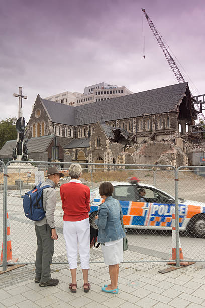 Christchurch Cathedral "Christchurch, New Zealand - March 4, 2013: Three tourists stand before the fenced remains of the Christchurch Cathedral at Cathedral Square, as a police car drives past. The landmark Anglican church was badly damaged in the February 2011 Christchurch earthquake and is still undergoing repairs two years on.." christchurch earthquake stock pictures, royalty-free photos & images