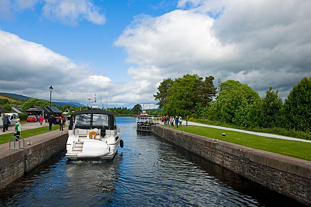 Fort Augustus "Fort Augustus, Scotland - June 11, 2010: Sluice gate in Fort Augustus, Scotland. A yacht leaves the sluice and goes in the Caledonian Canal. Many tourists stand there, and watch. The Caledonian Canal connecting Fort William to Inverness passes through Fort Augustus in a dramatic series of locks stepping down to Loch Ness." fort augustus stock pictures, royalty-free photos & images