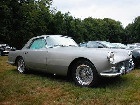 Apeldoorn, The Netherlands - August 31, 2003: Grey Ferrari 250 GT Pininfarina Coupe classic sports car parked on a grass field with other sports cars and classic cars.