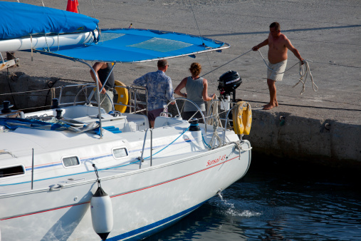 Mugla, Turkey- September 15, 2012: Sunsail43 named sailing boat moored at ferry dock in Datca. Tourist mature man was operating boat. Turkish man on the dock threw rope to man who’s standing deck of boat