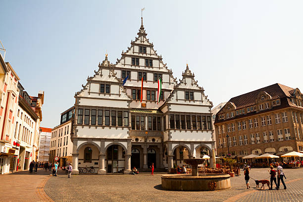 Town hall Paderborn "Paderborn, Germany - May, 1st 2012: Sunny spring day in center of Paderborn with old town hall in center of capture. Town hall is landmark of Paderborn. On square are walking and passing by some people in any direction. At right side is a cafA with tables outside. On square is small fountain." paderborn stock pictures, royalty-free photos & images