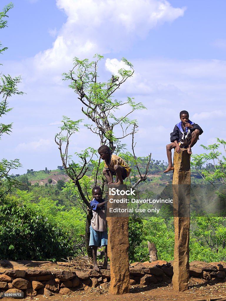 Kids of Konso "Konso, Ethiopia - November 4, 2012: Two boys sitting on wags, traditional hero statues while the third one is standing by on small wall. In background is surrounding vegetation, with small hill and blue cloudy sky above it." Africa Stock Photo