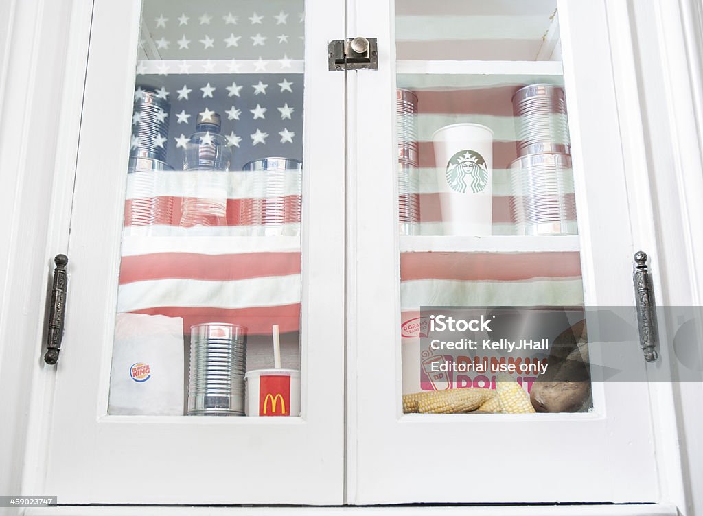 Fast food in America "Cincinnati, USA - April 4, 2013: A kitchen cabinet with canned goods, corn syrup, corn, potatoes, Starbucks, McDonalds, Burger King, Dunkin Donuts, and a reflection of the American flag." American Culture Stock Photo