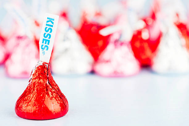 Hershey Kisses Candy for Valentine's Day "Suffolk, Virginia, USA - January 11, 2013: A horizontal studio shot of a Hershey Kisses chocolate candy wrapped in red foil for Valentine's Day. Defocused in the background are more of the chocolate candies, wrapped in bright red and silver foil." hersheys kisses stock pictures, royalty-free photos & images