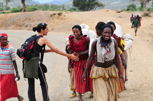 Konso, Ethiopia - August 9, 2010: An Israeli woman traveling in Ethiopia greets local villagers with a culturally correct handshake, in which one's left hand rest on the inside of the elbow during the handshake. The women are on their way to the market.