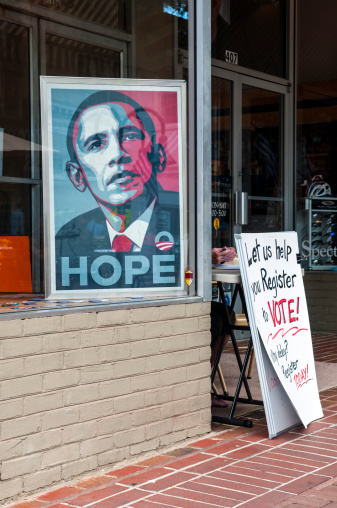 Charlottesville, Virginia, USA - June 7, 2012: An image of Barack Obama sits in a window. The hands of a woman operating a voter registration drive are visible behind the sign that reads 