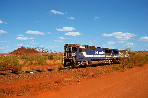 BHP train loading iron ore at Yandi mine "Newman, Australia  September 9, 2002:  BHP diesel locomotives at the head of an ore train as it loads iron ore for export at BHPs Yandi mine, 90km from the town of Newman.  In the background twin conveyors add ore to the large red stockpiles waiting to be loaded onto a train. In September 2008, BHP briefly suspended mining operations in the Pilbara after two fatalities at the Yandi mine." outback photos stock pictures, royalty-free photos & images