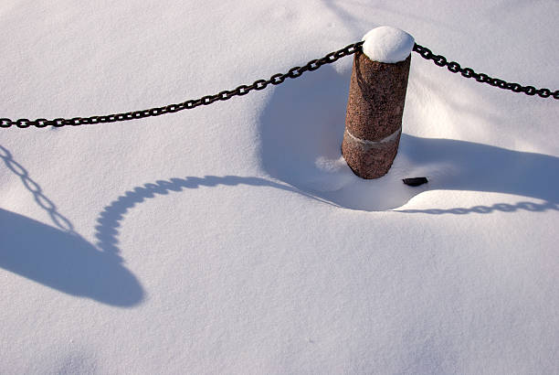 granite street bollard with metal chain in winter snow
