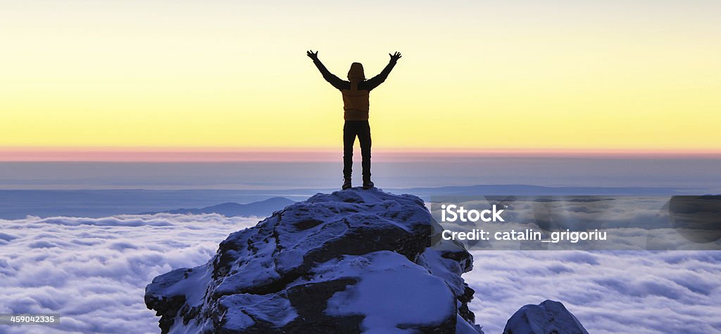 succes on top of the mountain hiker enjoys success of the ascent on top of the mountain with his hands in the air. below there is a sea of clouds in the morning sunrise light Mountain Peak Stock Photo