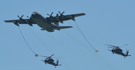 A U.S. Air Force C-130 Hercules doing a mid-air refueling of to UH-60 Blackhawk helicopters.
