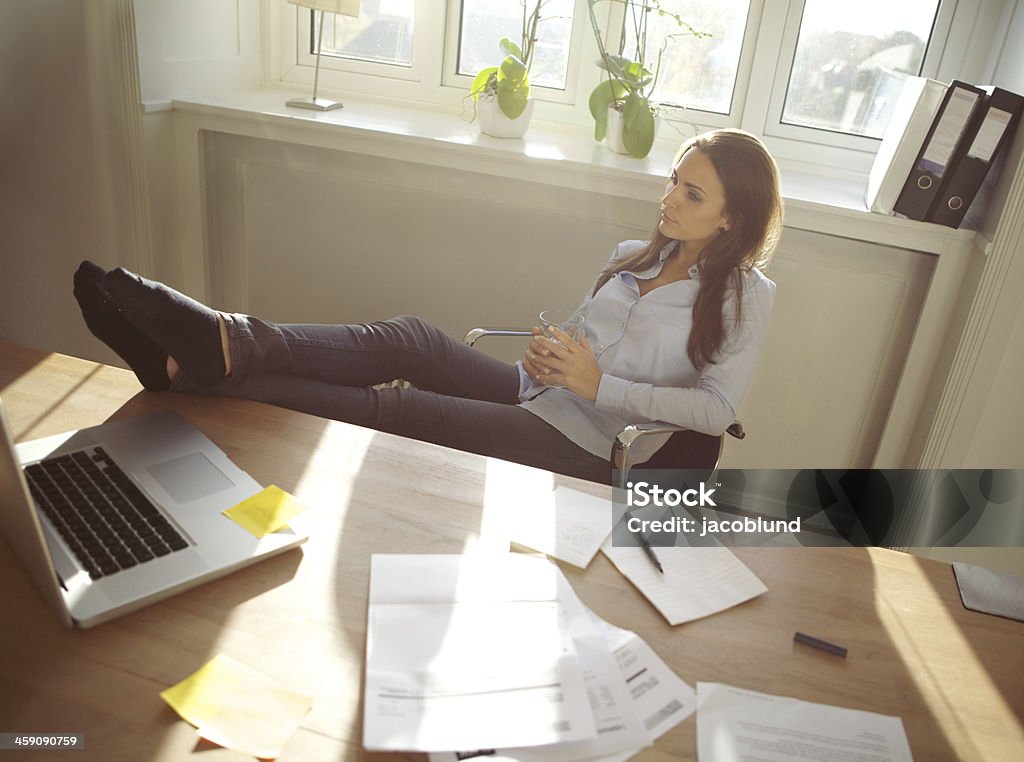 Young woman taking a break from work Young beautiful businesswoman at table resting with her legs on desk. Thoughtful caucasian female relaxing at her desk. Young woman taking a break from work at home office. 20-24 Years Stock Photo
