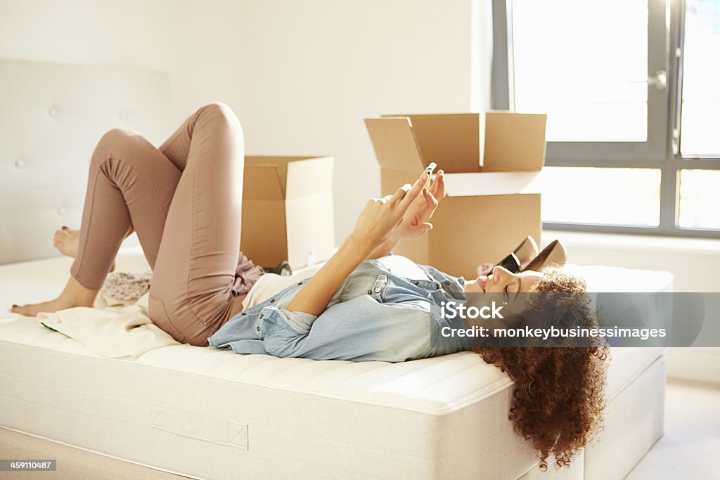 Woman Sending Text Message Having Moved Into New Home Woman Layed Down Sending Text Message Having Moved Into New Home 20-29 Years Stock Photo