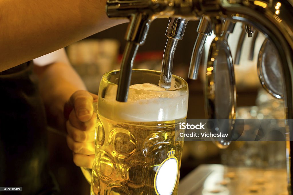 Dispensing draught beer in a pub Close up of a male bartender dispensing draught beer in a pub holding a large glass tankard under a spigot attachment on a stainless steel keg Beer - Alcohol Stock Photo