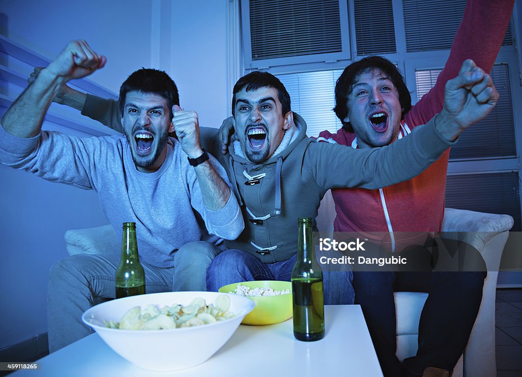 Friends watching sports on TV A group of friends are watching television.  They have their arms thrown into the air, and there are snacks and beer on the table in front of them. Domestic Life Stock Photo