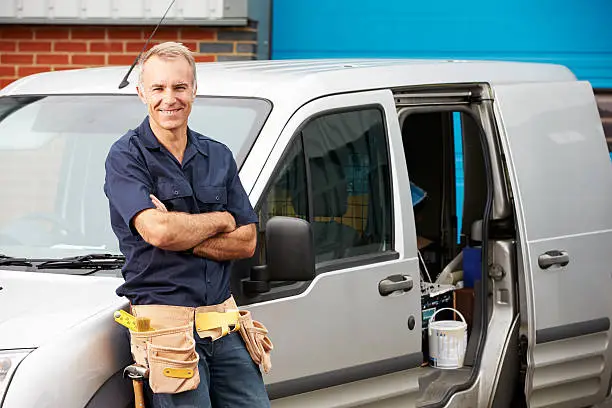 Plumber Or Electrician Standing Next To Van Smiling At Camera