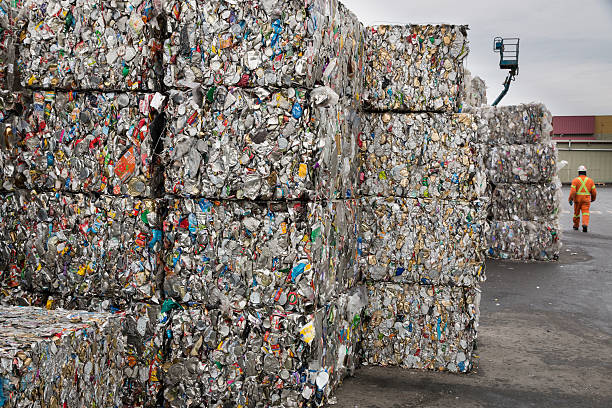 Cubes of recyled cans Victoria B.C , Canada- December 10, 2013: An unidentified worker, at a recycling collection facility, walks past stacks of metal cubes made from crushed tin cans, that await shipping to a recycling plant. aluminum plant stock pictures, royalty-free photos & images