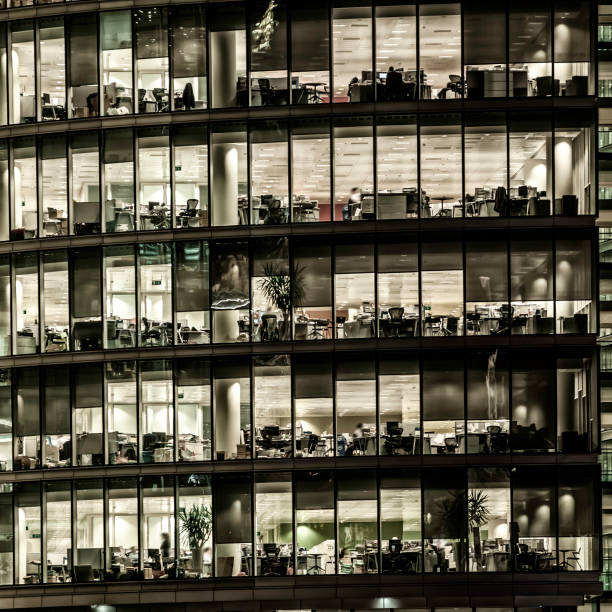 istock Office building at night with people working - III 459151619