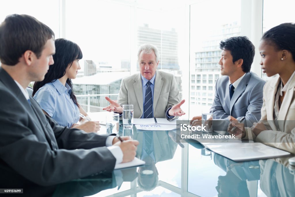 Mature businessman talking seriously to his employees A mature businessman talking very seriously to his younger employees Discussion Stock Photo