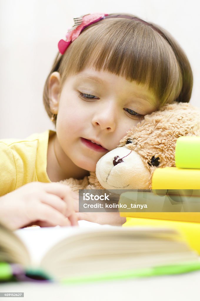 child reading Cute little girl with her toy bear are reading a book while sitting at table Book Stock Photo