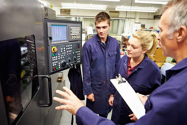 Trained Engineer Teaching Apprentices To Use Computerized Lathe At Work