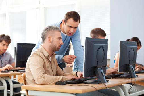 Group of adult students attending computer course. Focus on teacher talking with an adult man.