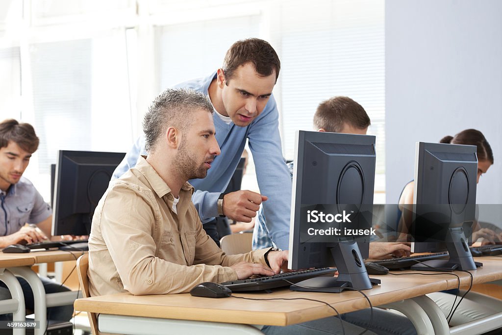 Adult education Group of adult students attending computer course. Focus on teacher talking with an adult man. Classroom Stock Photo
