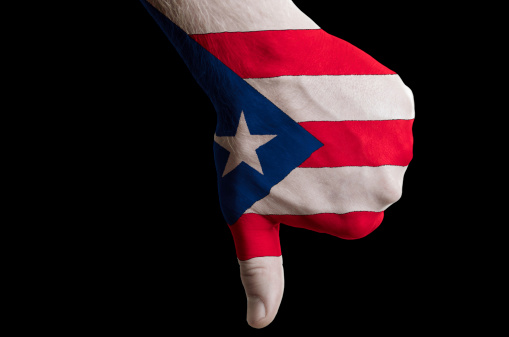 Hand with thumbs down gesture in colored puerto rico national flag as symbol of negative political, cultural, social management of country
