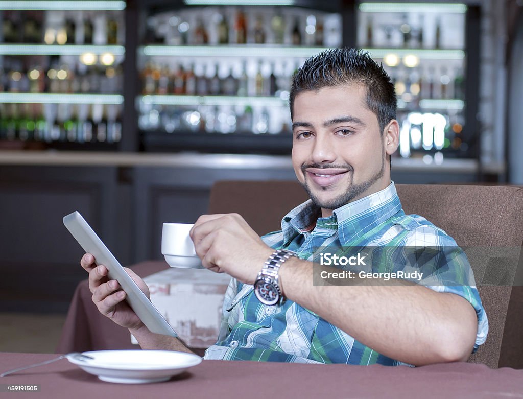 Cafe A young Indian guy in a cafe working on tablet Adult Stock Photo