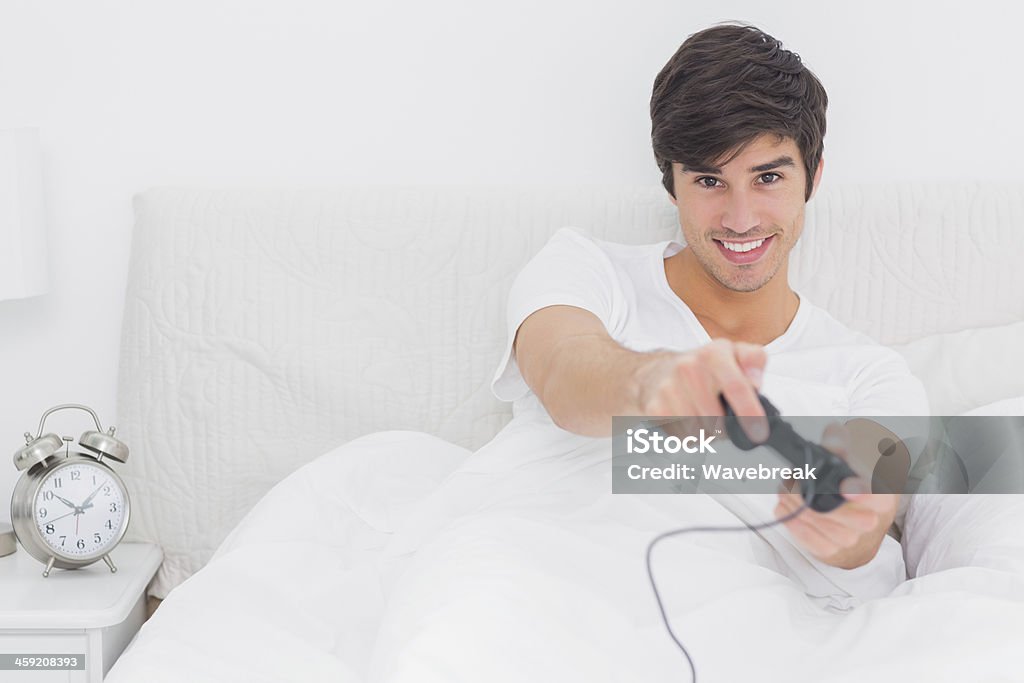 Jovem feliz homem sentado na cama, jogar jogos de vídeo - Foto de stock de Jogo de lazer royalty-free