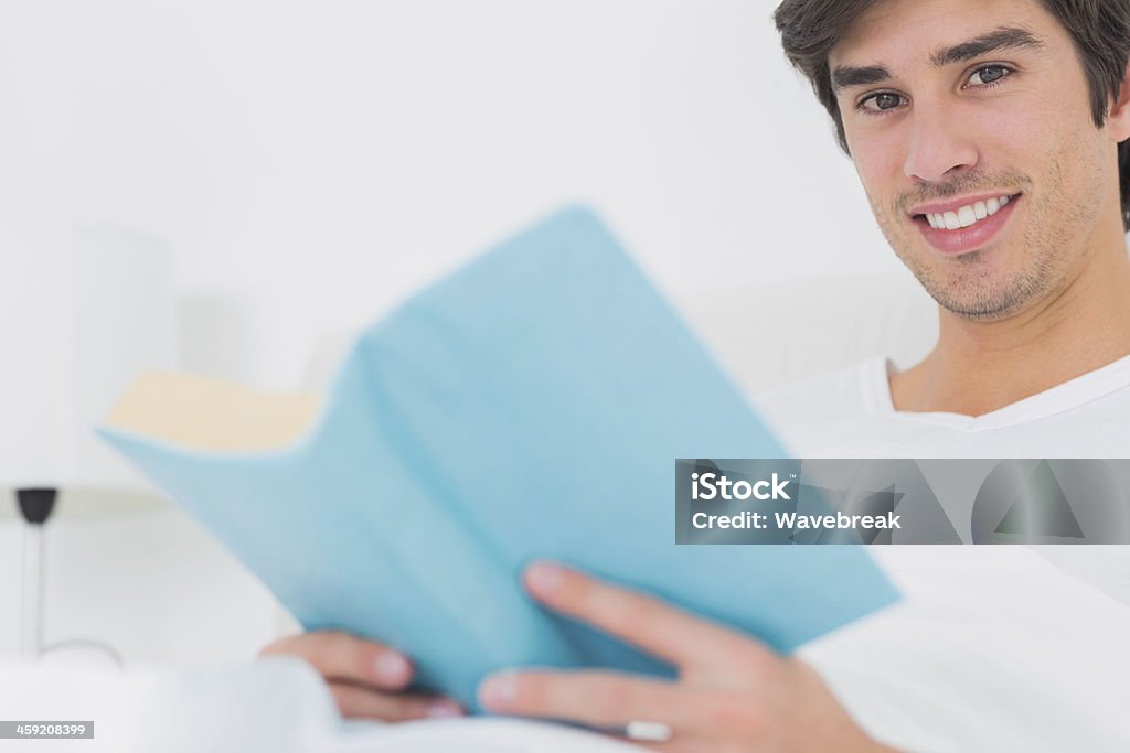 Fröhlich Mann Sitzen im Bett lesen Buch Blick in die Kamera - Lizenzfrei Bett Stock-Foto