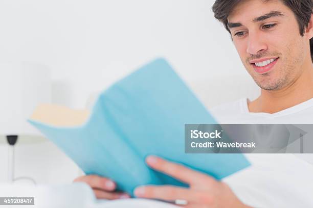 Alegre Homem Sentado Na Cama A Ler Livro - Fotografias de stock e mais imagens de 20-29 Anos - 20-29 Anos, Adulto, Almofada - Artigo de Decoração